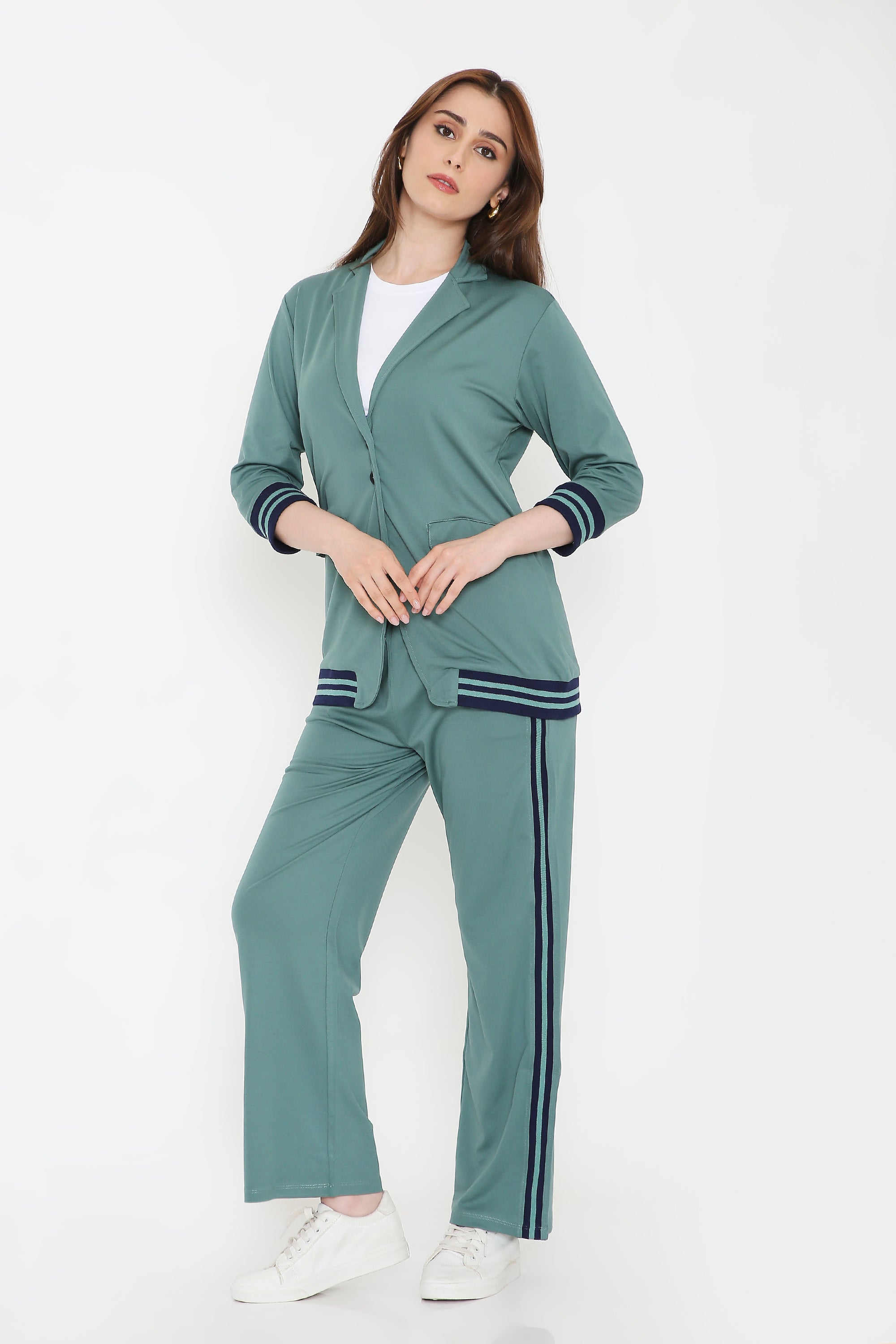 Model wears the Sage Green Athleisure Blazer Jacket and Track Set with navy stripes, paired with a white shirt and sneakers, posing against a white background.