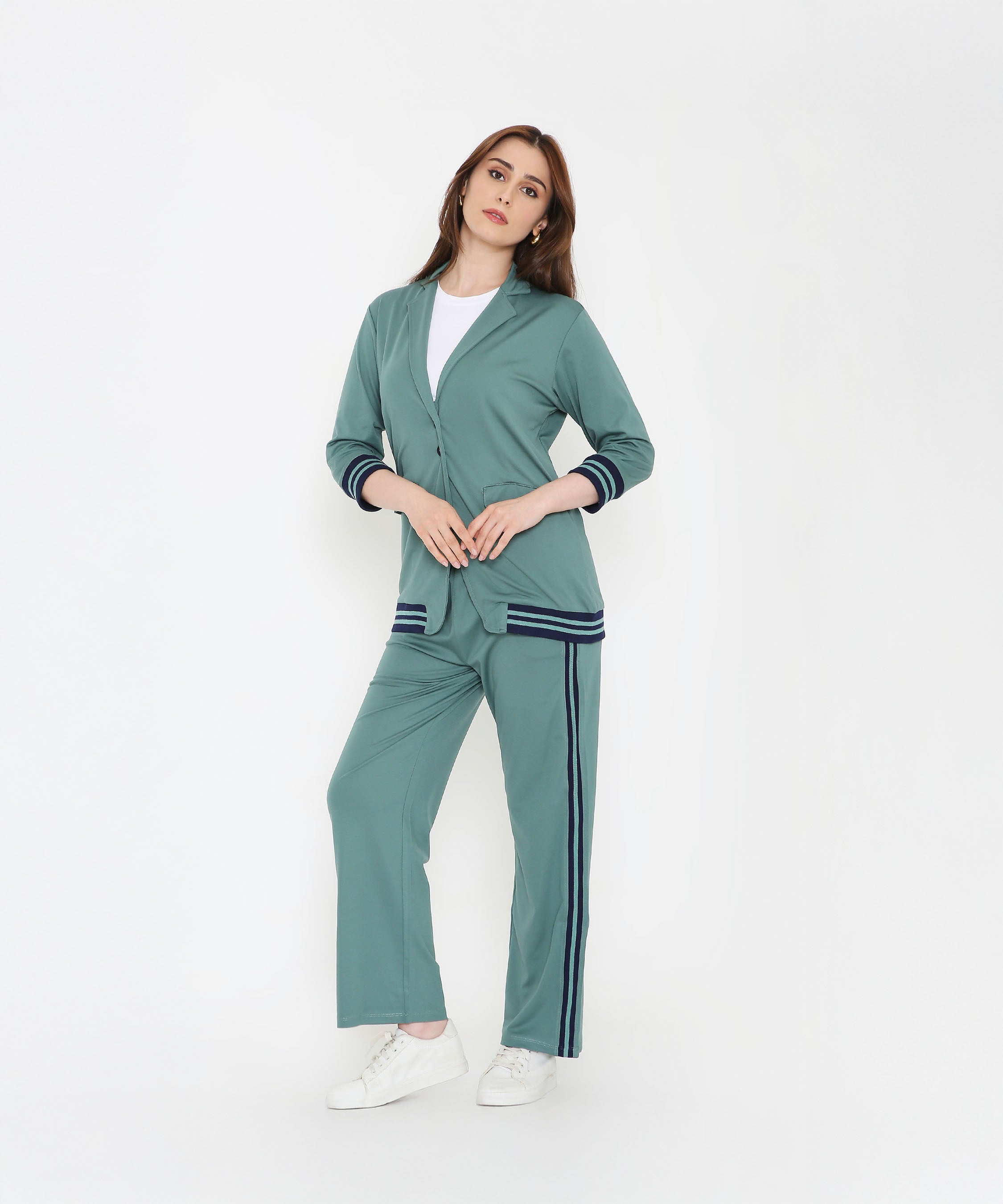 Model wears the Sage Green Athleisure Blazer Jacket and Track Set with navy stripes, paired with a white shirt and sneakers, posing against a white background.