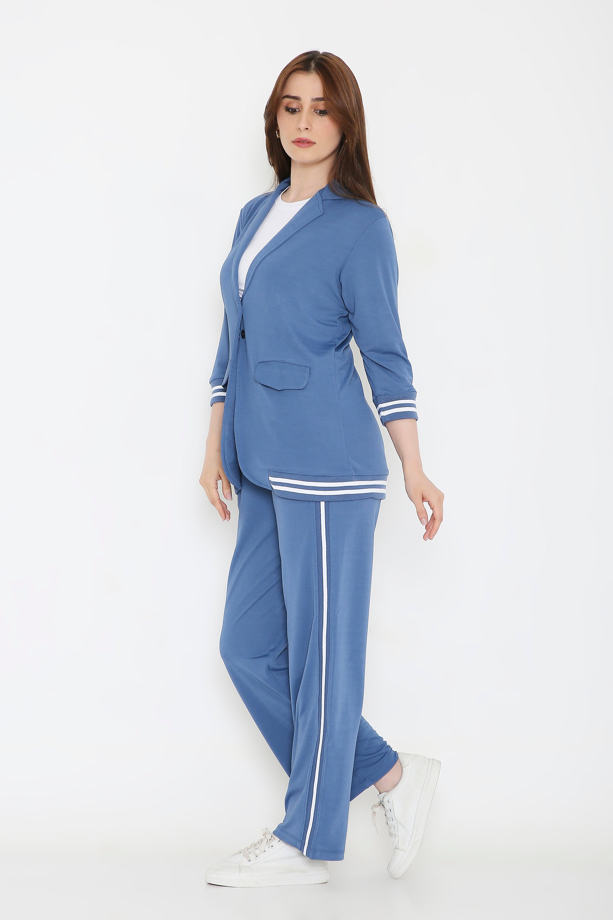 A woman stands confidently in the Atlantic Blue Athleisure Blazer Jacket and Track Set with white stripes and white sneakers against a plain white background.