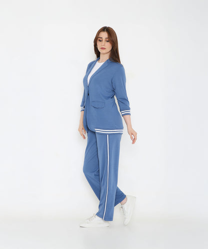 A woman stands confidently in the Atlantic Blue Athleisure Blazer Jacket and Track Set with white stripes and white sneakers against a plain white background.