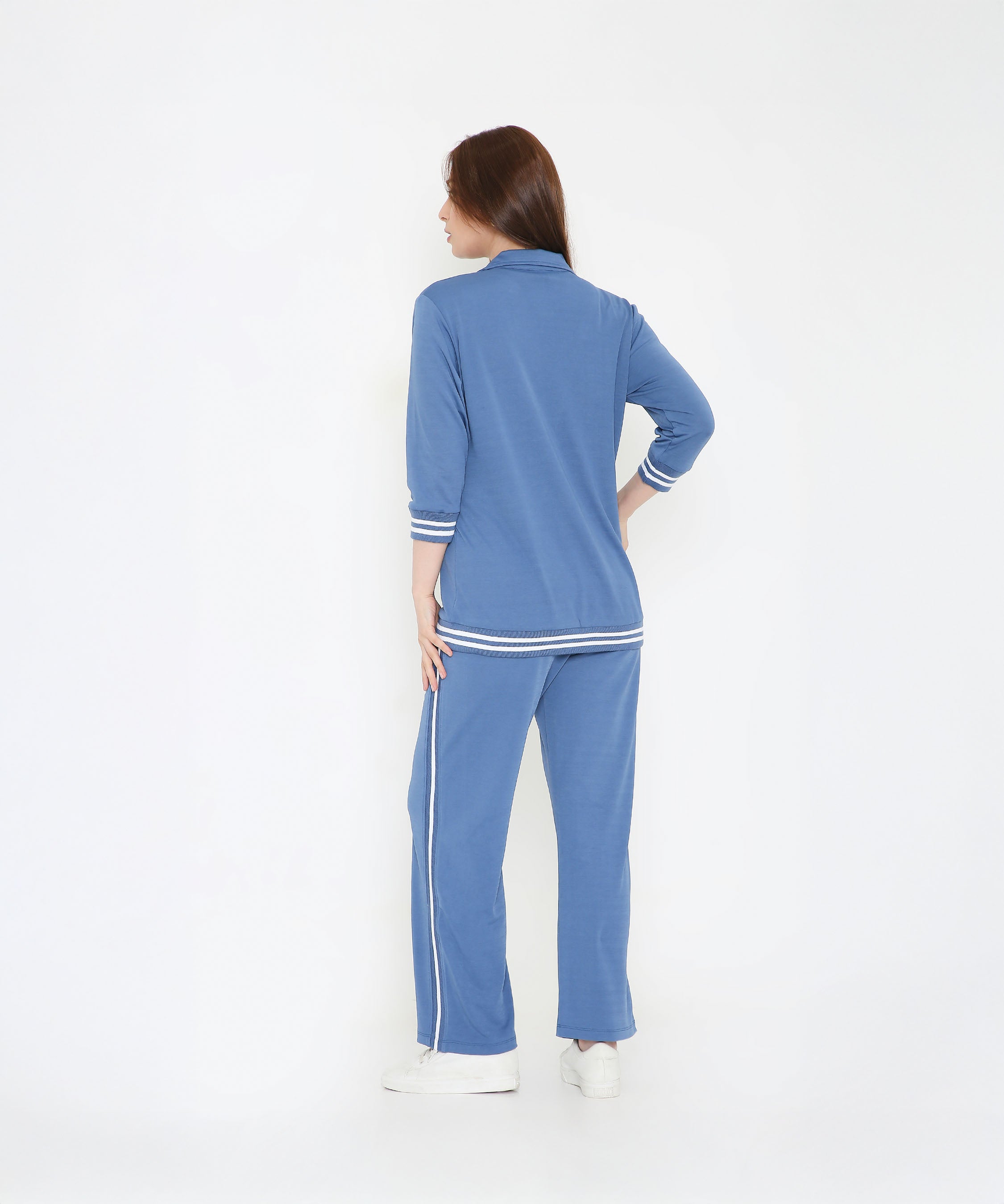 A woman faces away in the Atlantic Blue Athleisure Blazer Jacket and Track Set, featuring white stripes, against a white background.