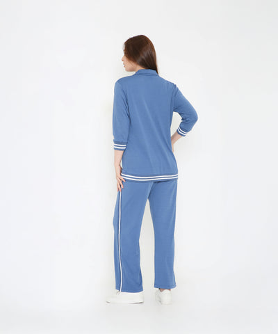 A woman faces away in the Atlantic Blue Athleisure Blazer Jacket and Track Set, featuring white stripes, against a white background.