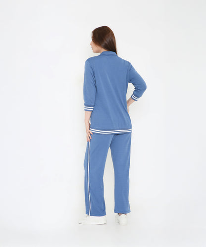 A woman faces away in the Atlantic Blue Athleisure Blazer Jacket and Track Set, featuring white stripes, against a white background.