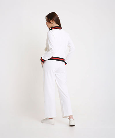 Woman sporting the Two Piece Bold Contrast White Tracksuit, featuring black and red trim on cotton-blend fabric, hands in pockets and facing away for a chic, modern look.