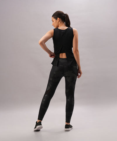 A woman models the Metallic Tie-Up - Top Only in black, featuring a shiny finish, standing with hands on hips and facing away against a plain light background.
