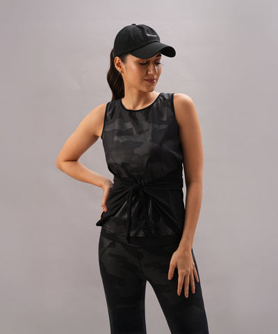 Woman wearing the Metallic Tie-Up - Top Only in black camo with a shiny finish and a cap, posing against a plain gray background.