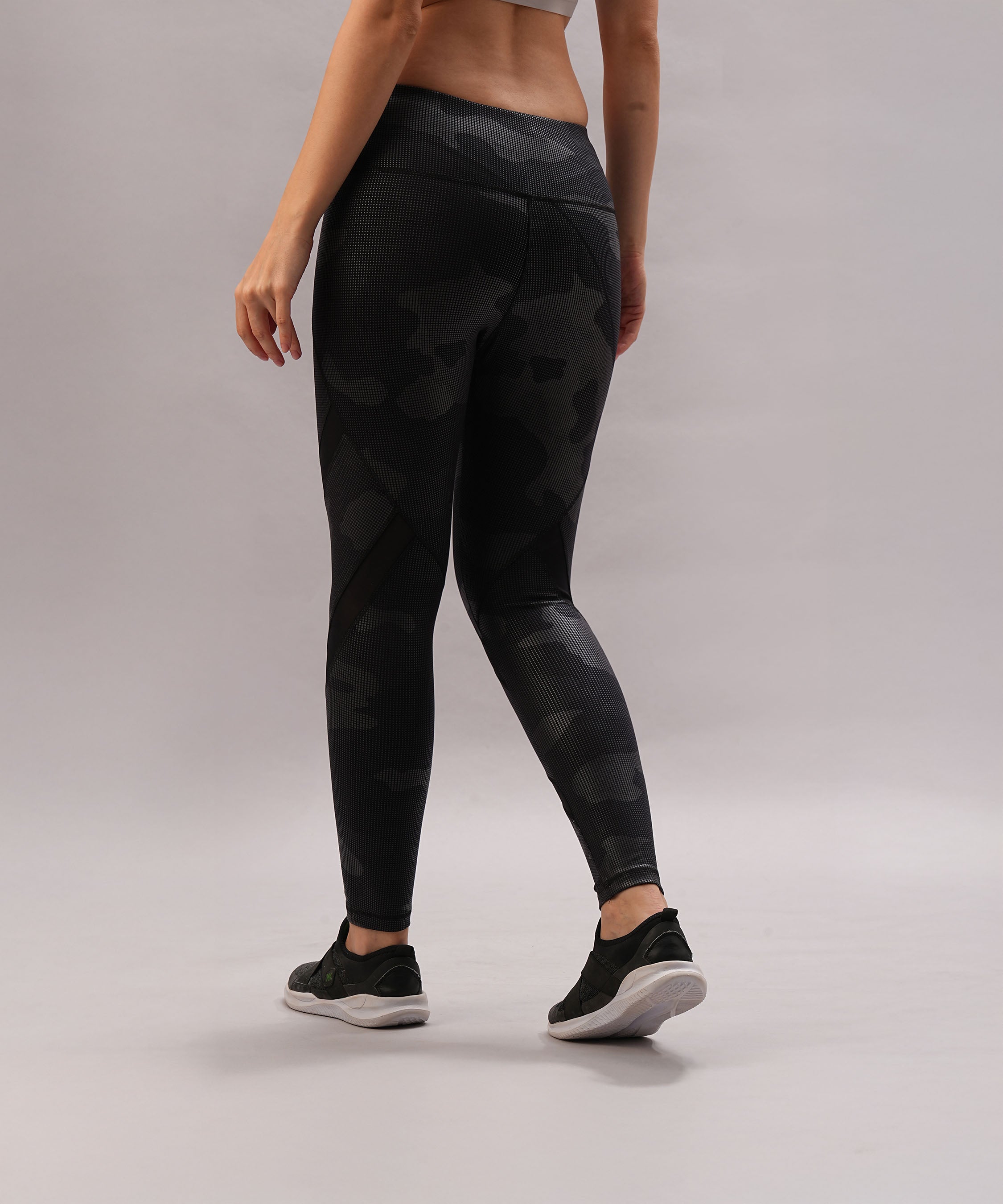A woman showcases Metallic Leggings with a stylish twist, paired with black sneakers, standing against a plain light gray background.