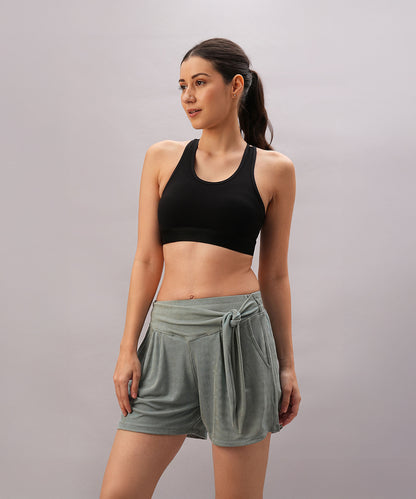 A woman wearing the Black Sports Bra with adjustable straps and green shorts stands against a plain background, looking to the side.
