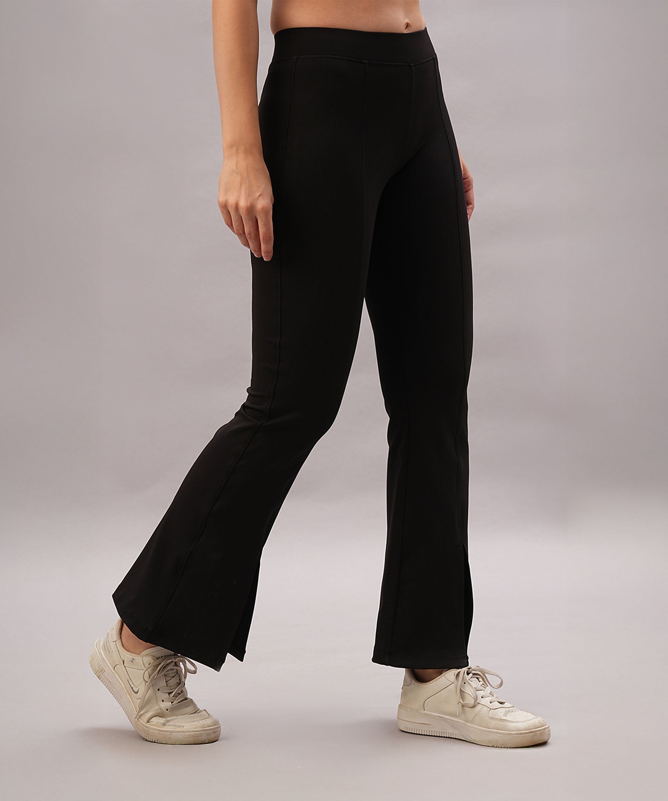 A person stands against a plain background wearing Black Slit Leggings and white sneakers.