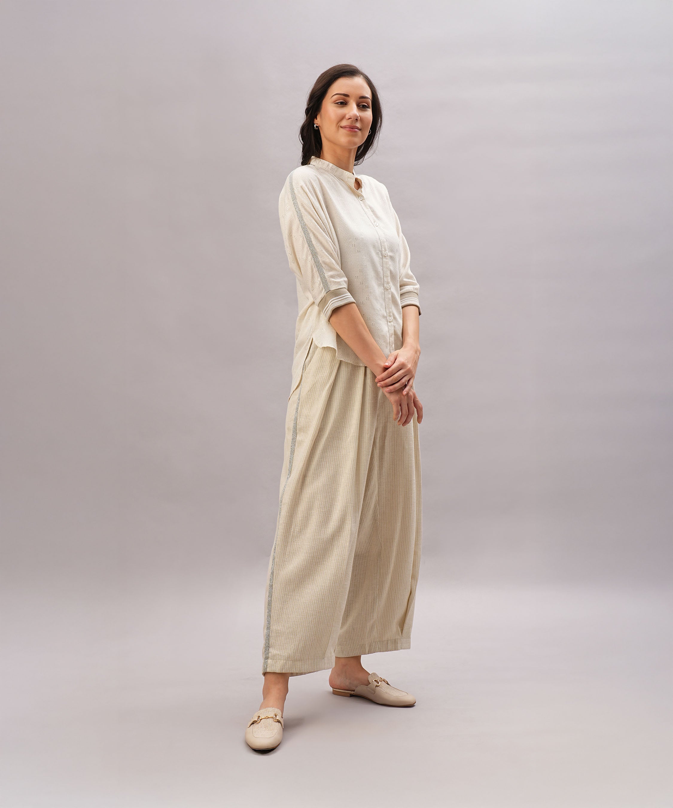 A woman stands smiling against a plain light gray background, showcasing the comfort and relaxed fit of the Beige Linen Set made from breathable linen.