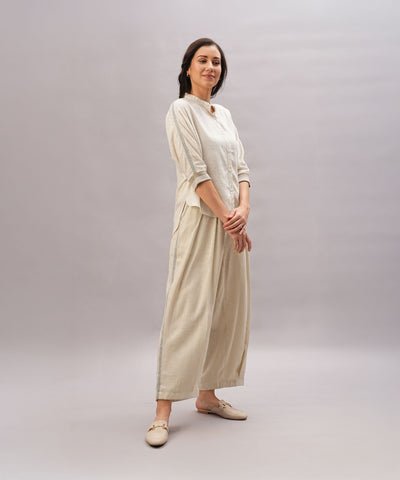 A woman stands smiling against a plain light gray background, showcasing the comfort and relaxed fit of the Beige Linen Set made from breathable linen.