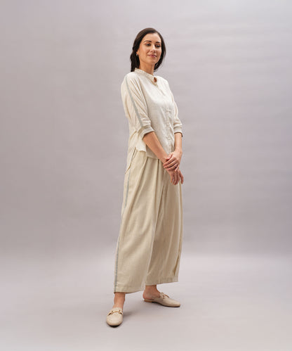 A woman stands smiling against a plain light gray background, showcasing the comfort and relaxed fit of the Beige Linen Set made from breathable linen.