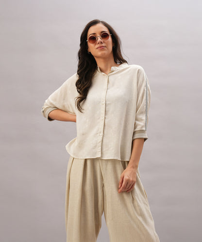 A woman in a relaxed fit Beige Linen Set and sunglasses poses confidently against a light gray background, highlighting the effortless elegance and breathability of the Beige Linen Set.