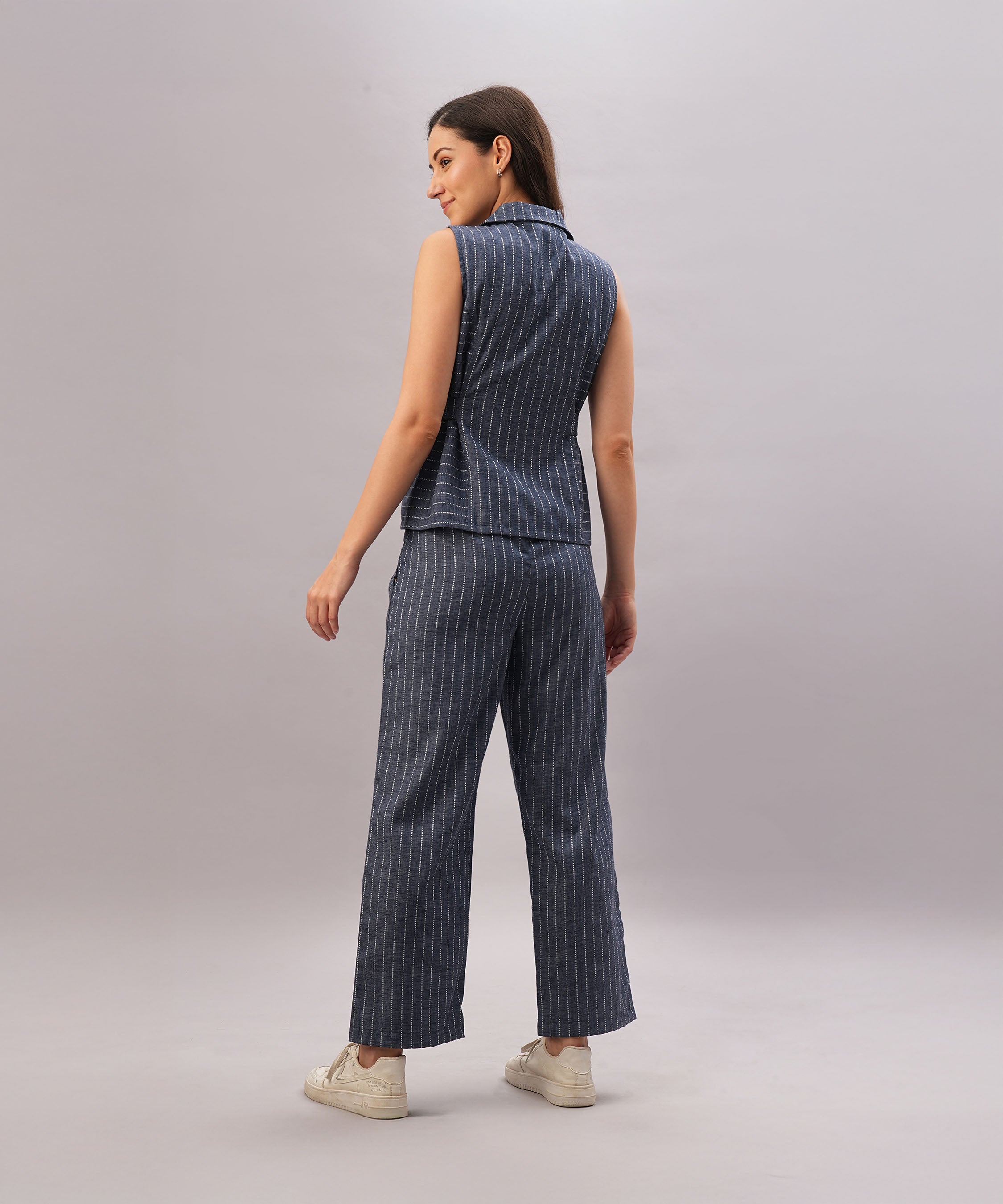 A woman models the Navy Blue Stripe Set—sleeveless top and pants in 100% cotton, featuring a comfortable fit. She stands sideways, facing away, paired with white sneakers.