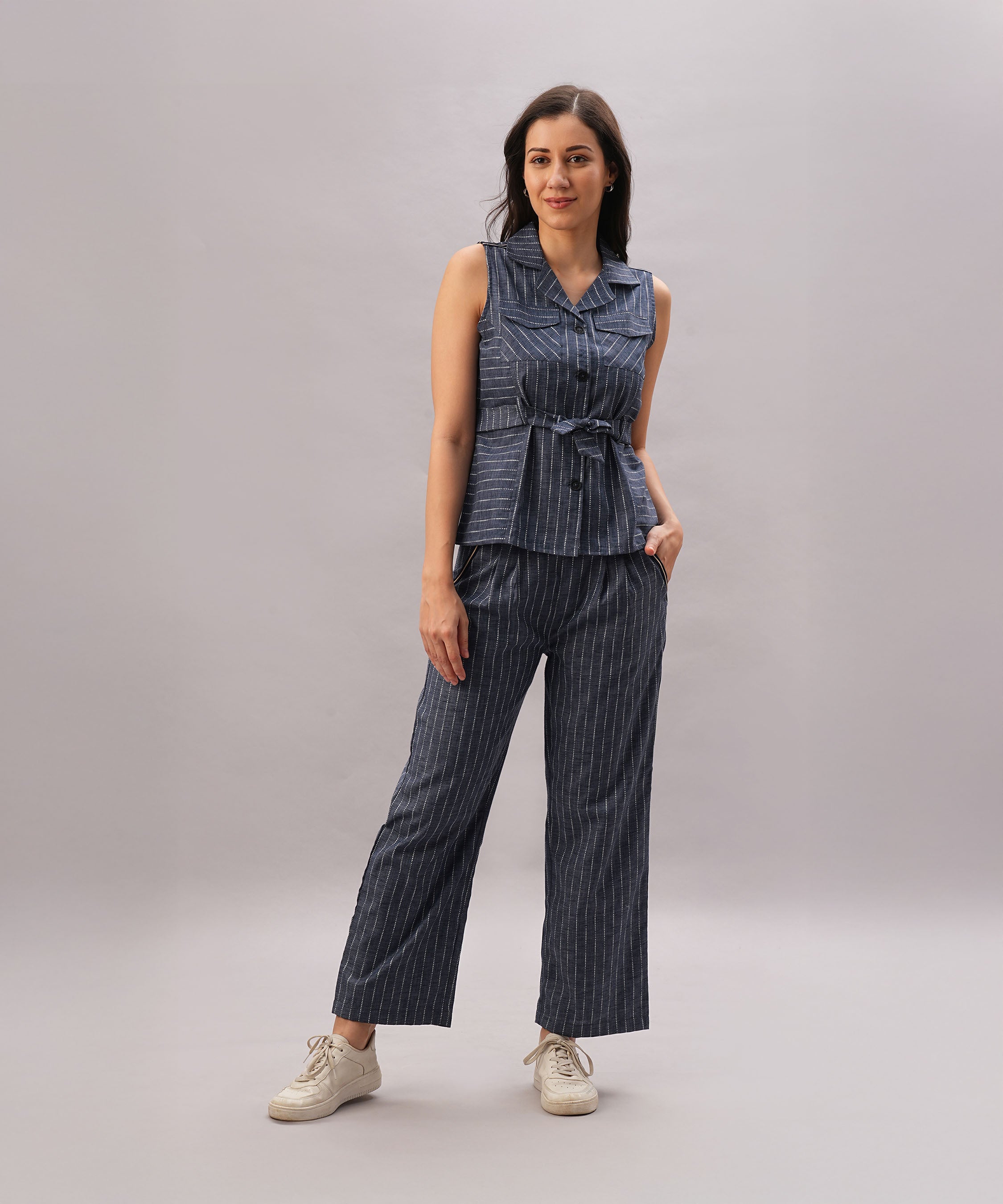 A woman smiles as she stands against a plain background, wearing the Navy Blue Stripe Set—a sleeveless outfit with a comfortable fit.