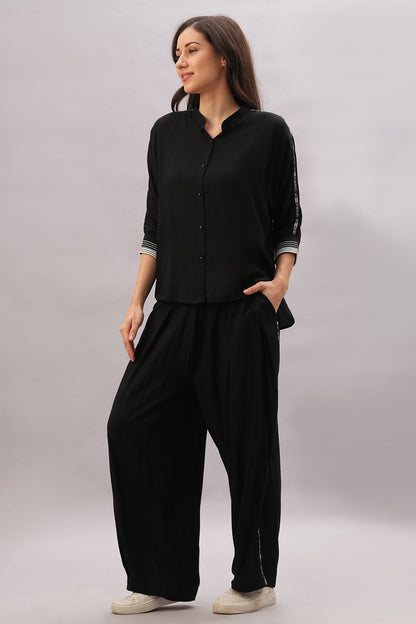 Woman wearing the Black Rayon Co-Ord Set with a chic top and loose-fit pants, standing with hands in pockets and paired with white sneakers.