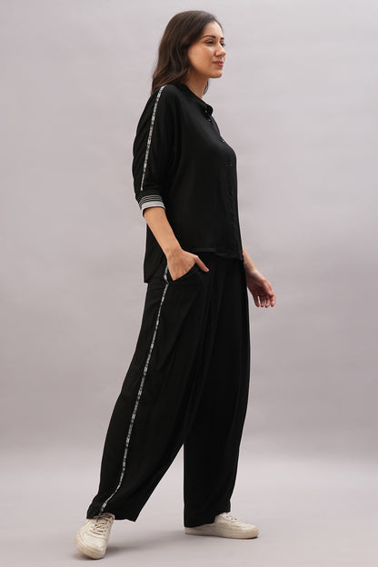 Woman wearing the Black Rayon Co-Ord Set with a stylish top and loose-fit striped pants, hands in pockets, paired with white sneakers.