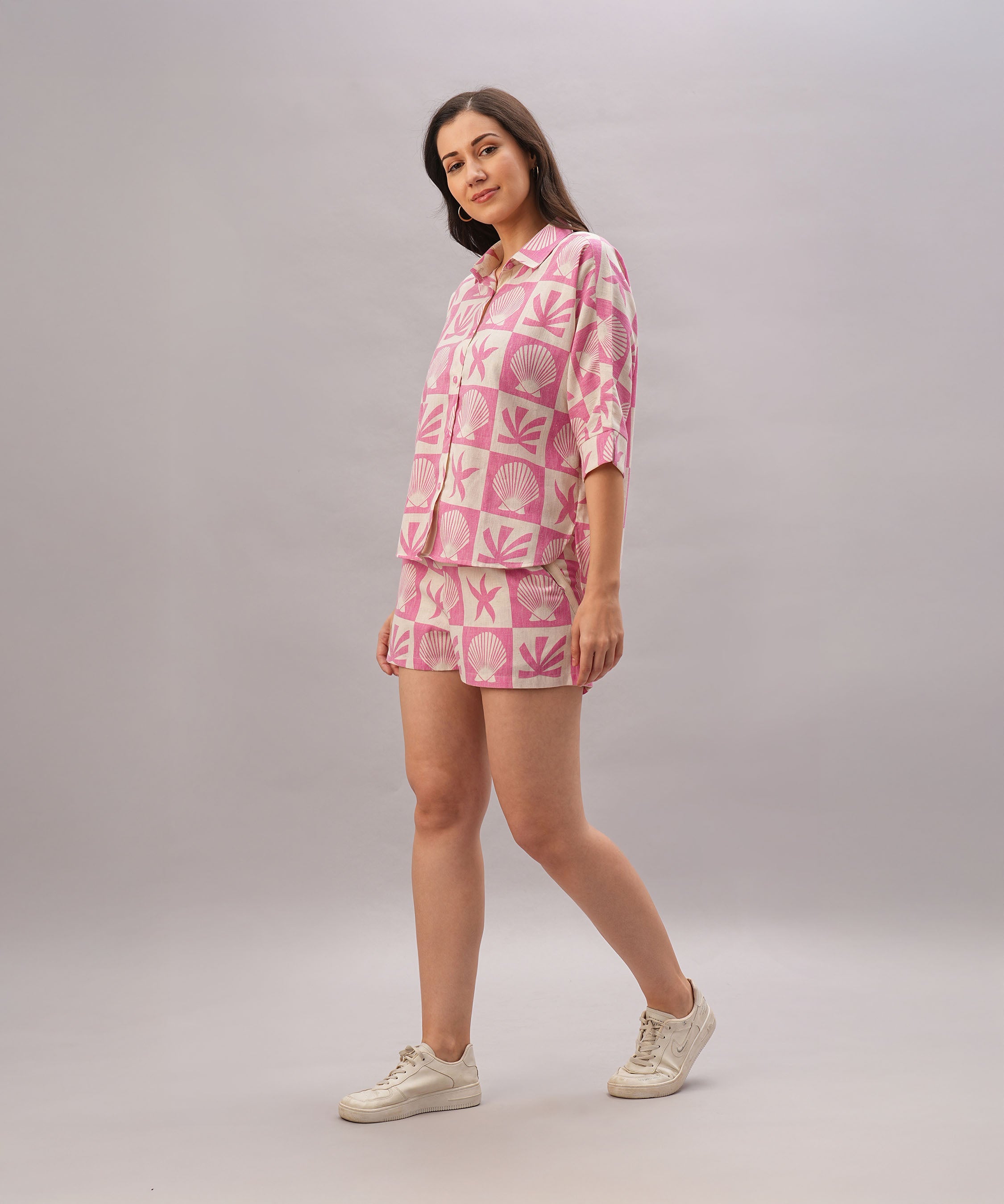 A woman wears the Pink Co-Ord set, which includes a trendy top and matching bottoms, as she walks and smiles against a plain light gray background.