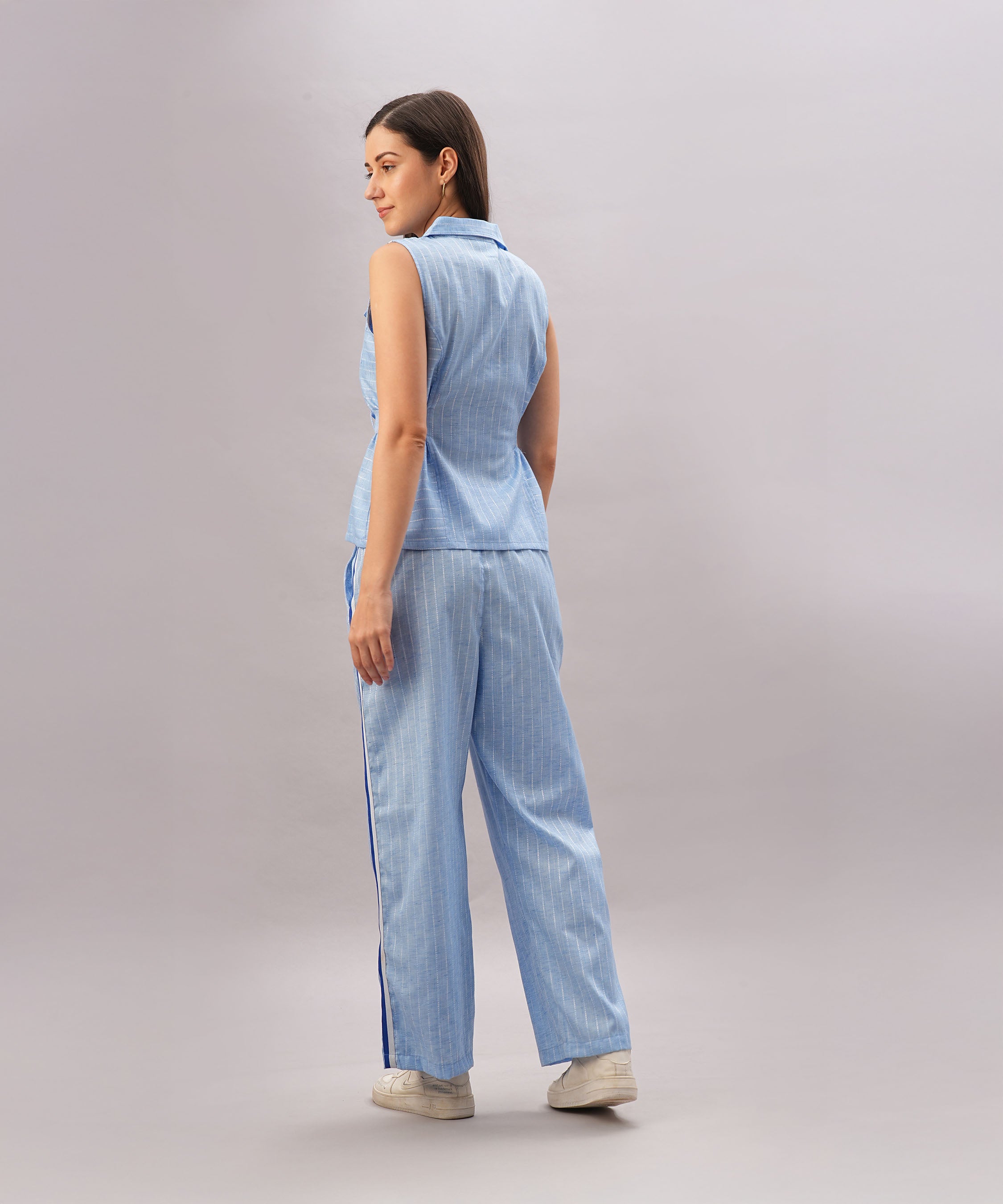 A woman in the Light Blue Stripes Co-Ord Set, featuring a sleeveless top and pants, stands facing away against a plain light background.