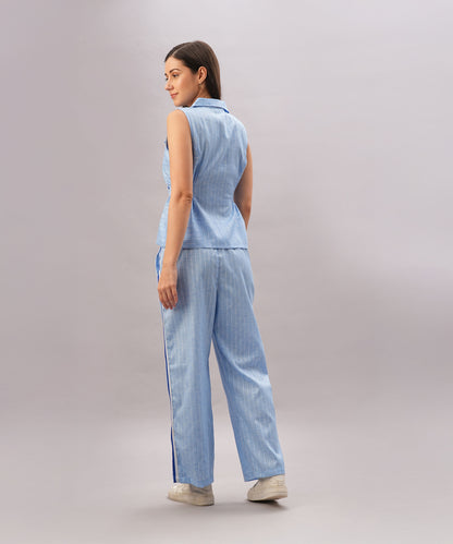 A woman in the Light Blue Stripes Co-Ord Set, featuring a sleeveless top and pants, stands facing away against a plain light background.