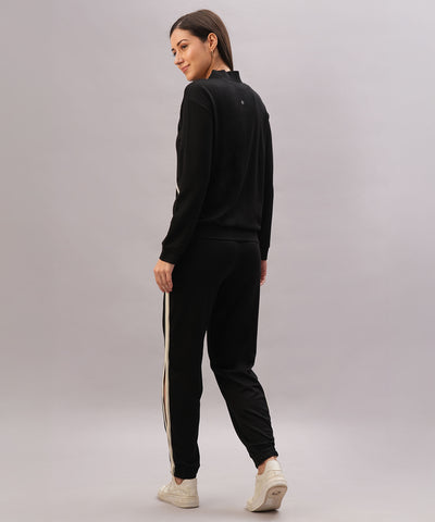 Woman stands against a plain background, looking back and wearing the Black Co-Ord Set made from soft cotton lycra, featuring white side stripes.