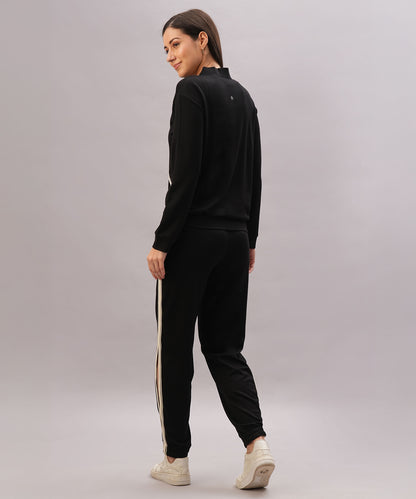 Woman stands against a plain background, looking back and wearing the Black Co-Ord Set made from soft cotton lycra, featuring white side stripes.