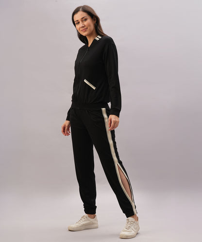 A woman stands smiling against a gray background wearing a Black Co-Ord Set with white stripes, made from cotton lycra, paired with white sneakers.