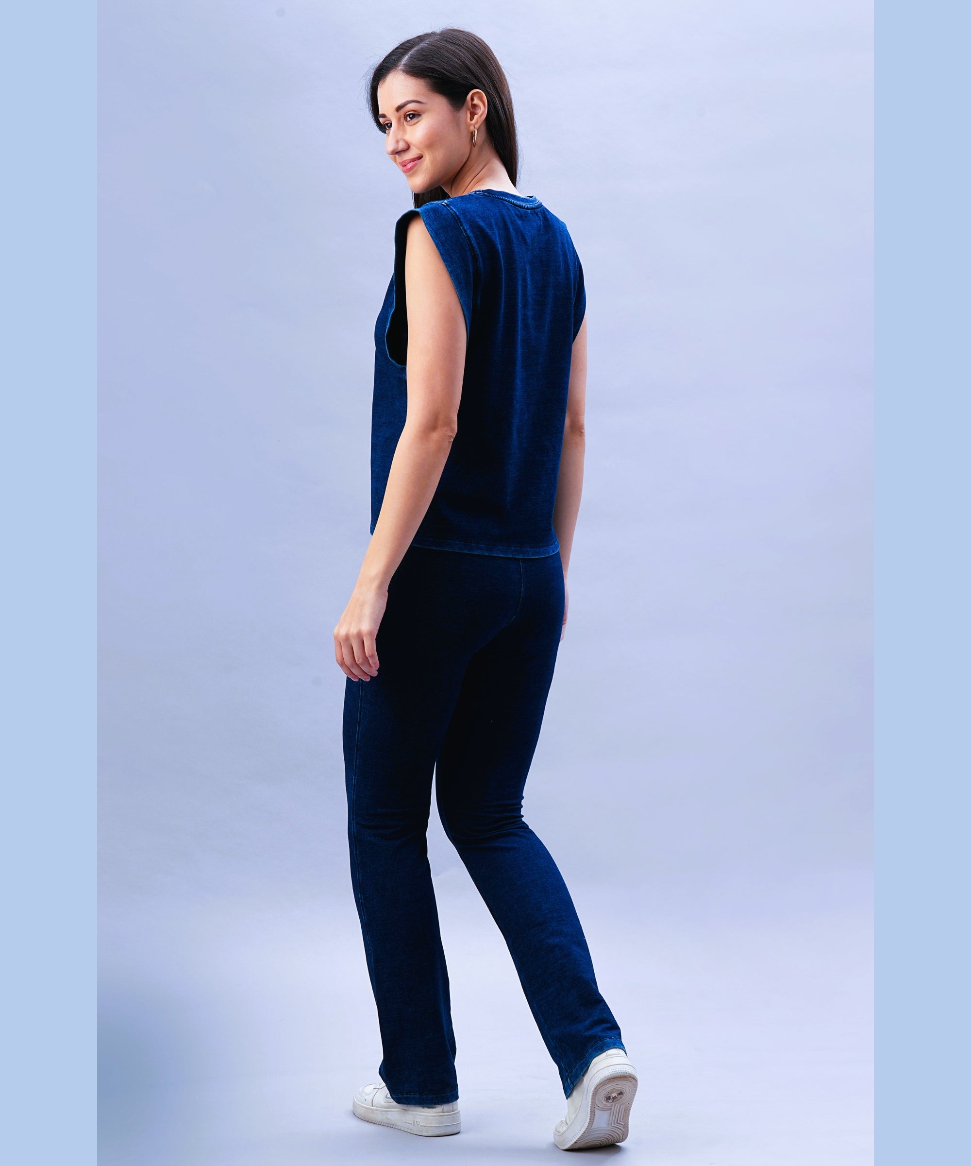 Smiling woman wearing a blue sleeveless top and Blue Denim Wash Bootcut Leggings with a high-rise waistband, looking over her shoulder against a light background.