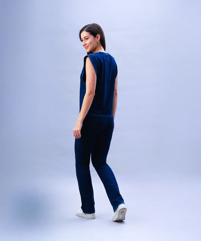 Woman in Blue Denim Wash Bootcut Leggings with a high-rise waistband and white sneakers, smiling and looking over her shoulder against a light background.
