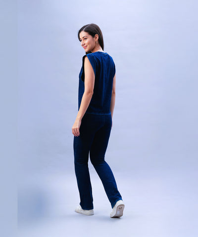 Woman wearing a Blue Denim Wash Capsleeves Top, looking over her shoulder while walking against a light background.