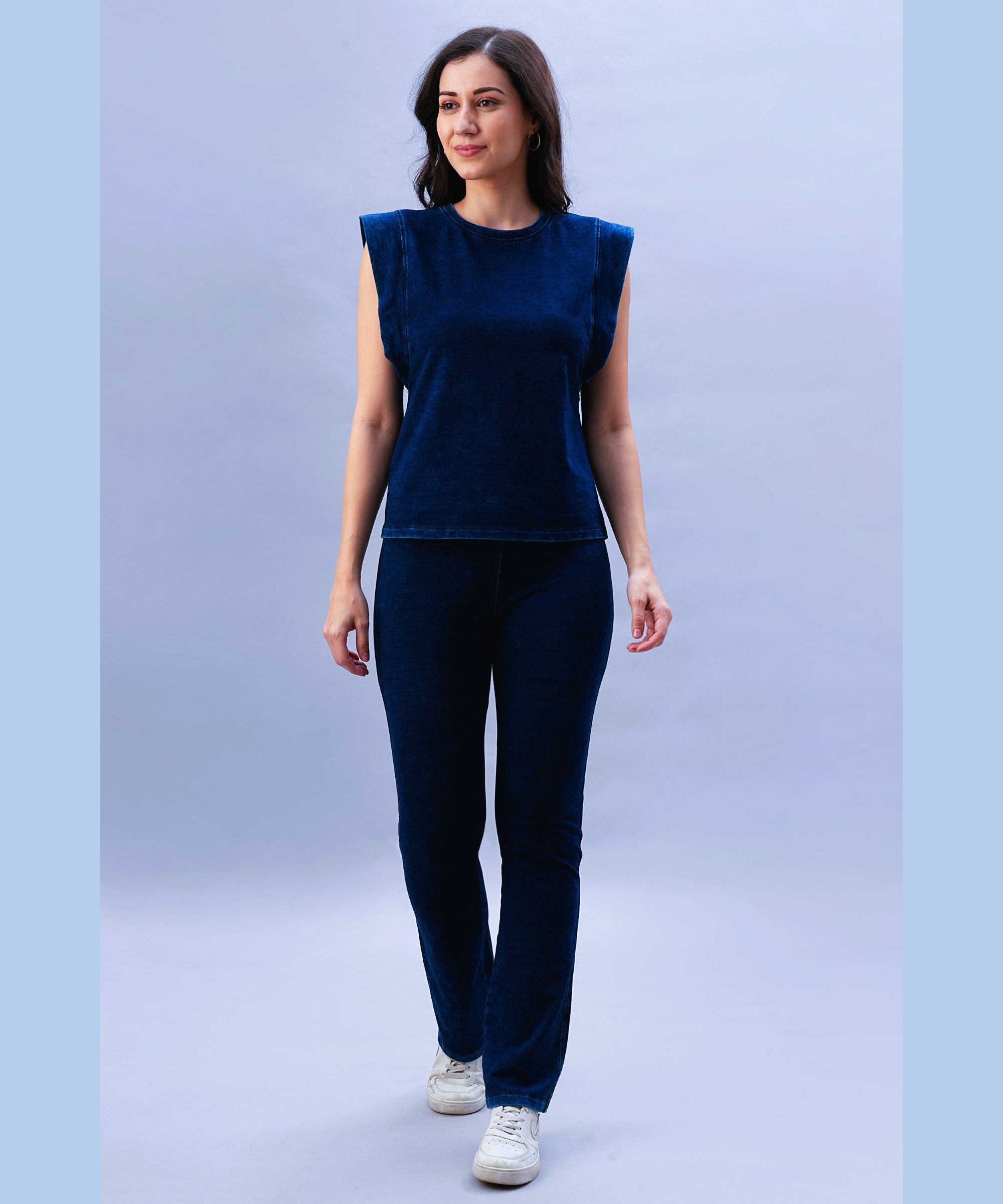 A woman wearing the Blue Denim Wash Capsleeves Top and matching pants walks and smiles against a light blue background.