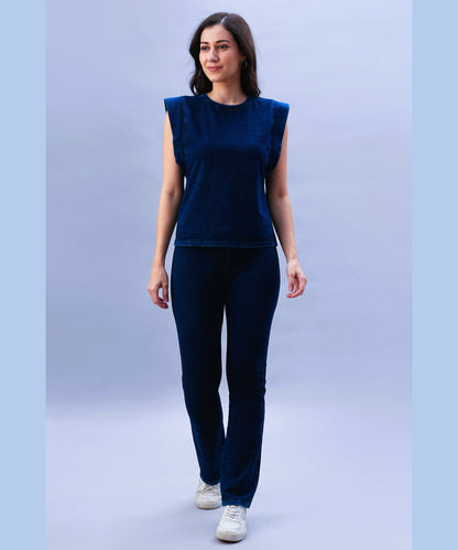A woman wearing the Blue Denim Wash Capsleeves Top and matching pants walks and smiles against a light blue background.