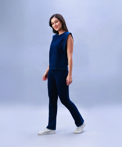 A woman stands and smiles against a plain light blue background, wearing a sleeveless blue top paired with Blue Denim Wash Bootcut Leggings featuring a high-rise waistband.