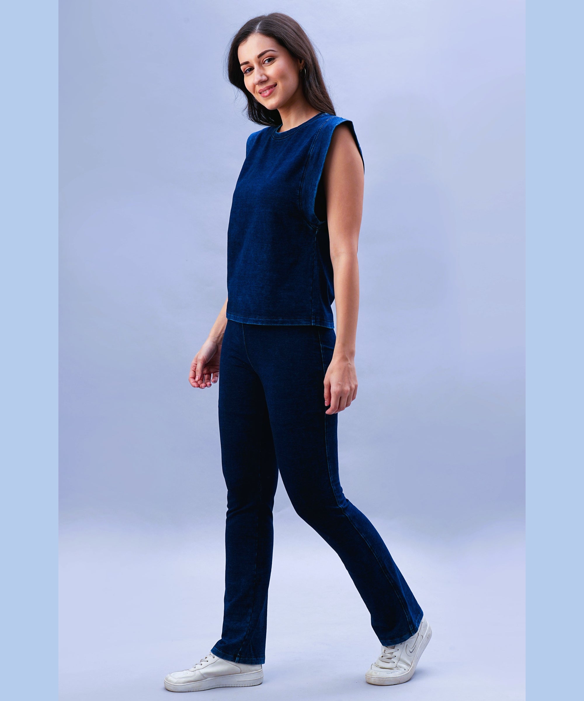 Woman in a dark blue velvet top and Blue Denim Wash Bootcut Leggings with a high-rise waistband, walking and smiling against a light blue background.