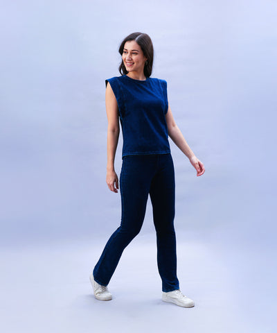 Woman smiling and standing against a plain light blue background, wearing the Blue Denim Wash Capsleeves Top.