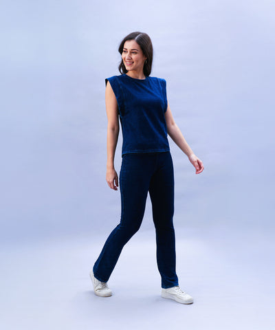 A smiling woman showcases the Blue Denim Wash Capsleeves Tops and Bootcut Leggings Set, featuring high-waisted bootcut leggings in stretchable fabric, paired with white sneakers against a light blue background.