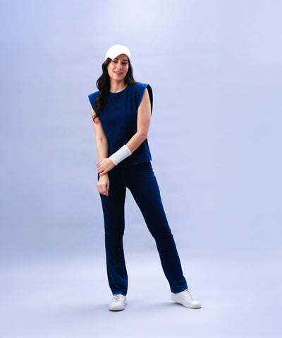 A woman in Blue Denim Wash Bootcut Leggings with a high-rise waistband and a white cap smiles and wears a white wristband against a light blue background.