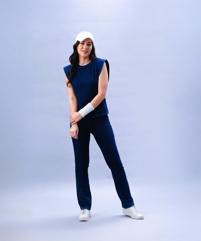 A woman wearing the Blue Denim Wash Capsleeves Tops and Bootcut Leggings Set with a white cap and sneakers smiles against a plain light background.