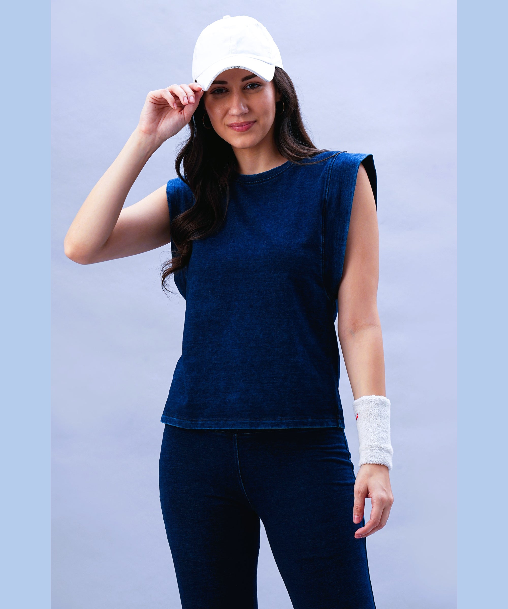 A woman in a Blue Denim Wash Capsleeves Top, blue pants, white cap, and wristband smiles at the camera.