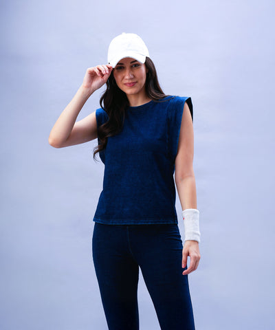Woman wearing the Blue Denim Wash Capsleeves Top with matching pants, a white cap, and wristband, standing against a light blue background.