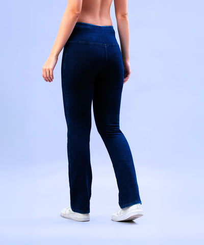 Wearing Blue Denim Wash Bootcut Leggings with a high-rise waistband and white sneakers, a person stands on a light blue background, viewed from behind.