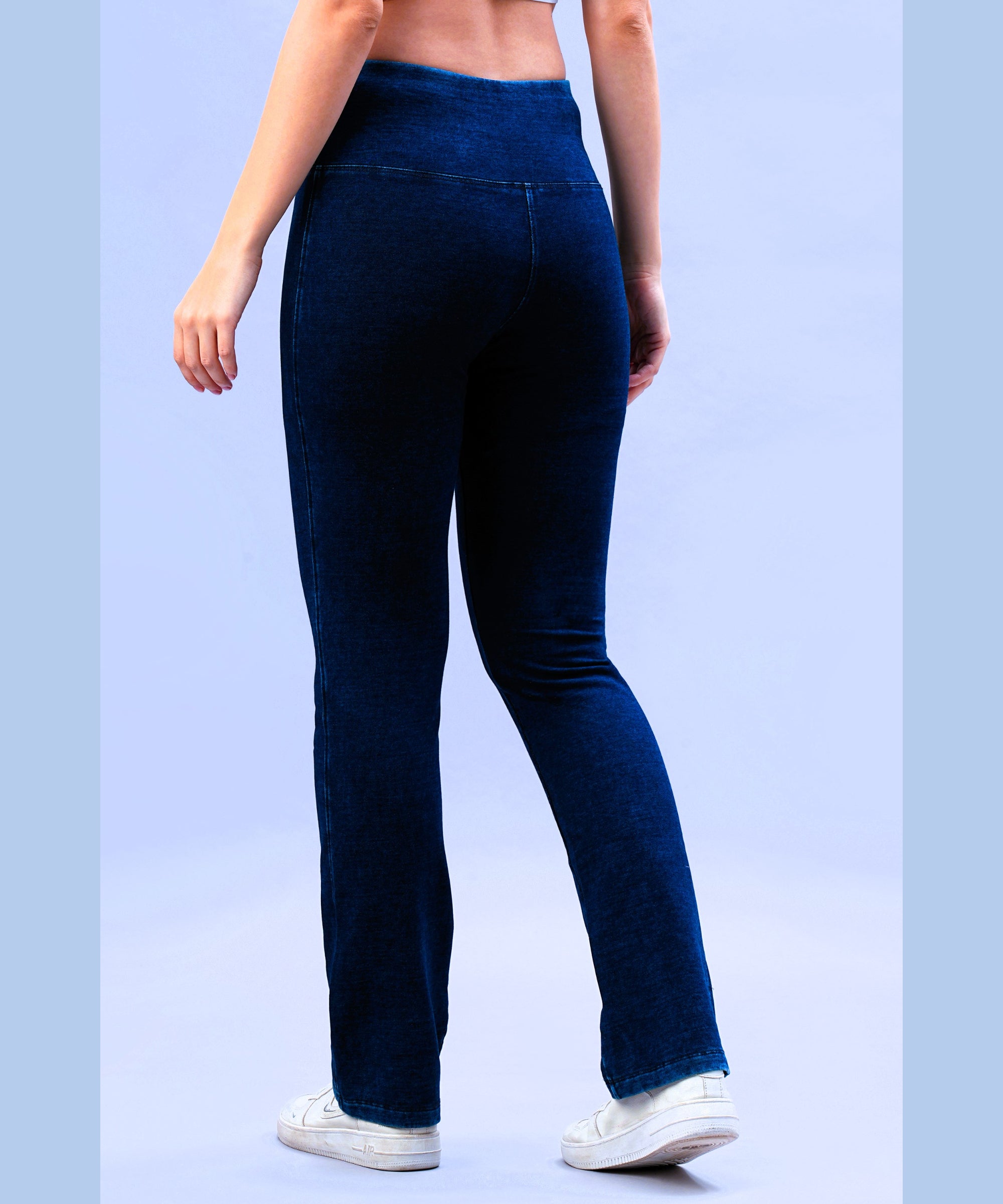 A person is seen from behind wearing Blue Denim Wash Bootcut Leggings with a high-rise waistband and white sneakers, standing against a light blue background.