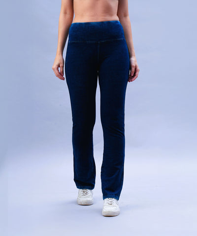 Woman wearing Blue Denim Wash Bootcut Leggings featuring a high-rise waistband and white sneakers, standing against a light blue background.