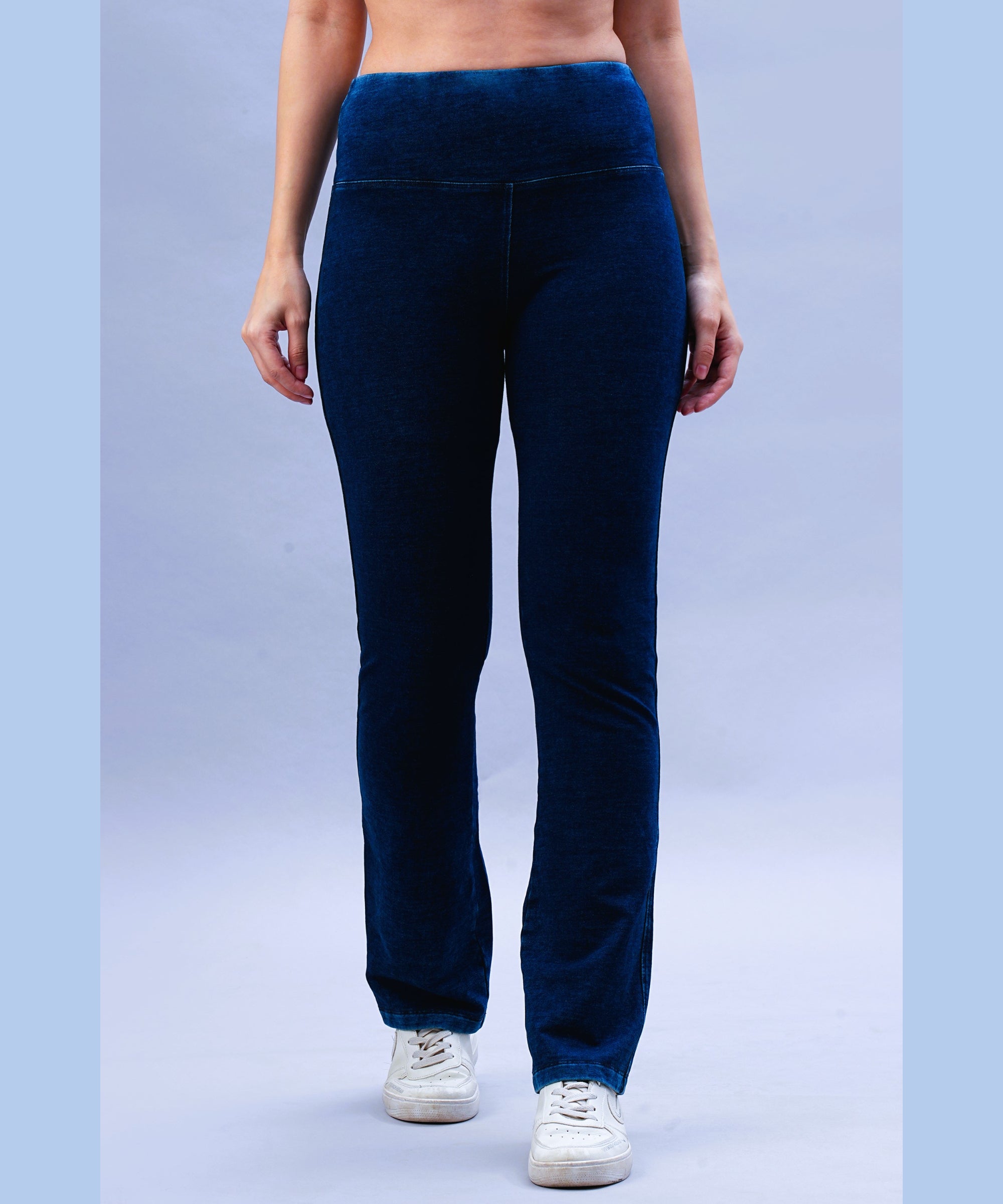 Someone wearing Blue Denim Wash Bootcut Leggings with a high-rise waistband and white sneakers stands against a light blue background.
