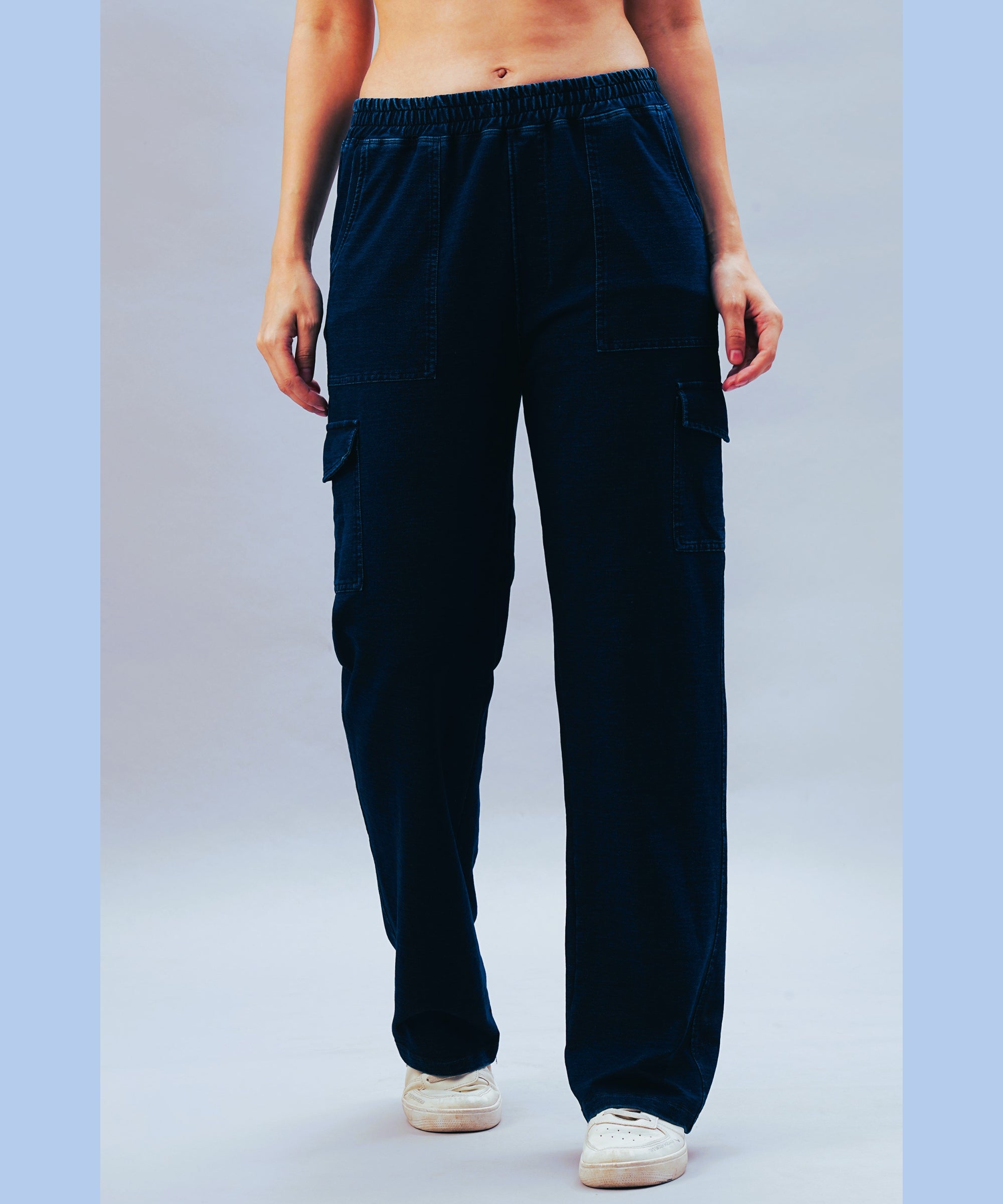 A person wearing the Blue Denim Wash Cargo Trackpant and white sneakers stands against a light blue background.
