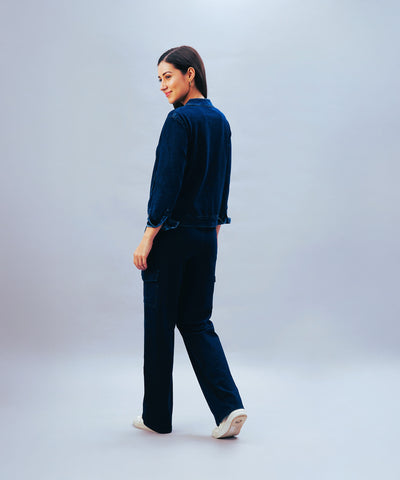 Woman in a dark blue outfit wearing Blue Denim Wash Cargo Trackpant and white shoes, standing and looking over her shoulder against a plain background.