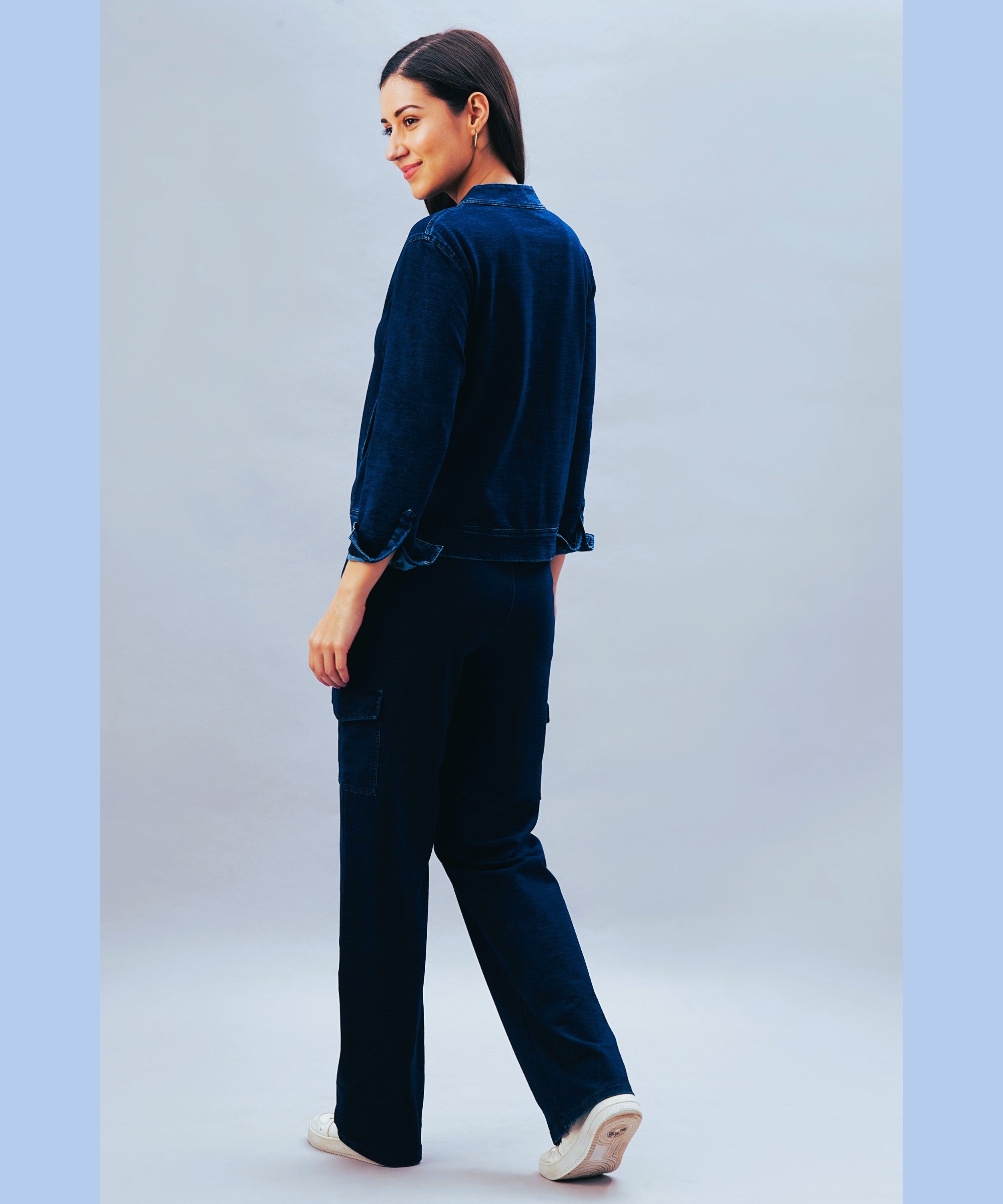 Smiling woman in a navy blue outfit poses against a light blue background, effortlessly styling the Blue Denim Wash Cargo Trackpant.