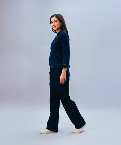 A woman wearing Blue Denim Wash Cargo Trackpant and white shoes stands against a plain, light background, looking to the side.
