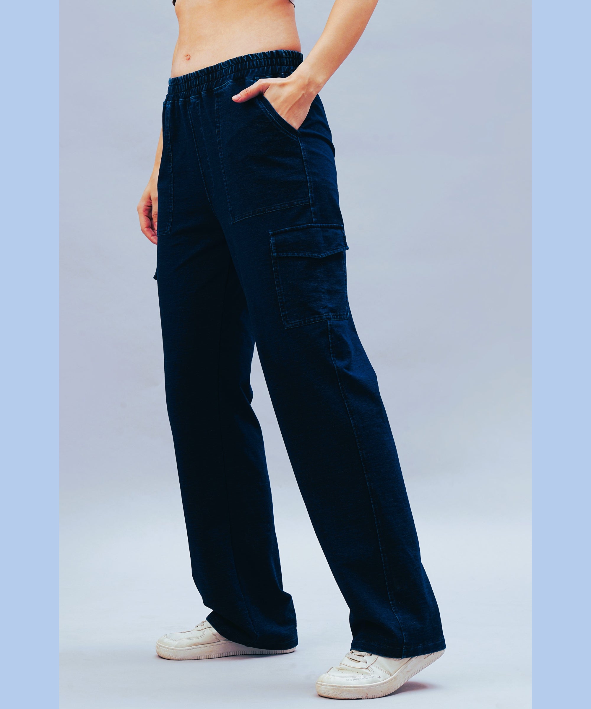 A person models the Blue Denim Wash Cargo Trackpant with white sneakers, hand in pocket, posed against a light background.