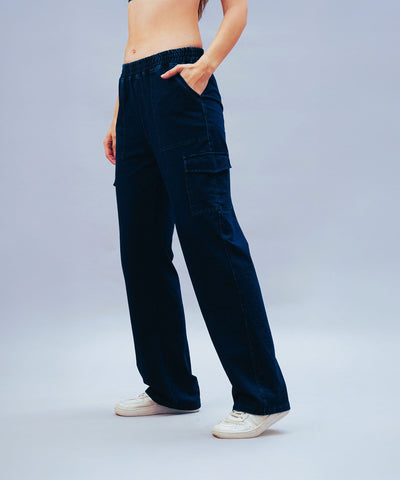 Person wearing Blue Denim Wash Cargo Trackpant and white sneakers, standing with one hand in pocket against a plain background.